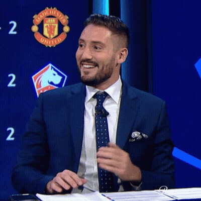 Man In Suit Smiling In Front Of Manchester United Sign GIF