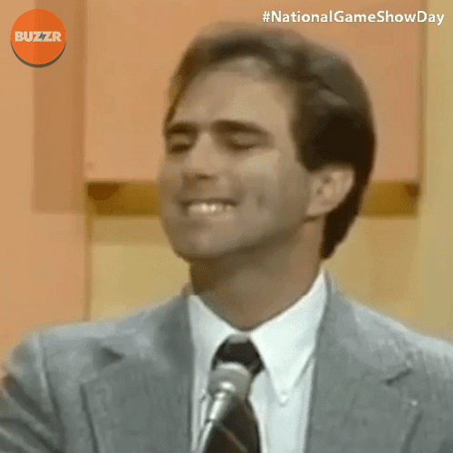 Man In Suit Smiling In Front Of Microphone With Buzzr Logo GIF