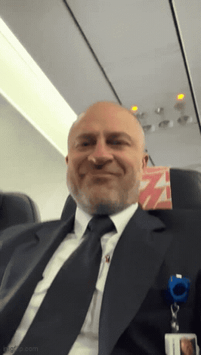 Man In Suit Smiling On Airplane GIF
