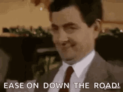 Man In Suit Smiling Says Ease On Down The Road GIF