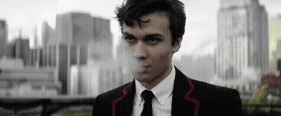 Man In Suit Smoking Cigarette In Front Of City GIF