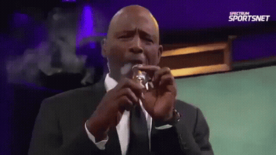 Man In Suit Smoking Cigarette In Front Of Spectrum Sportsnet Sign GIF