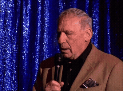 Man In Suit Speaking Into Microphone Blue Curtain GIF