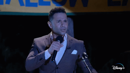 Man In Suit Speaking Into Microphone In Front Of Disney+ Sign GIF