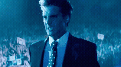 Man In Suit Standing Before Crowd In Dark Room GIF