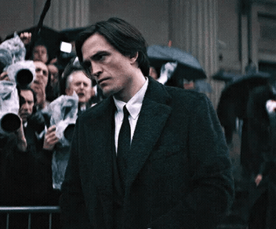 Man In Suit Standing Before Crowd With Umbrellas GIF