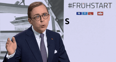 Man In Suit Standing Before #Fruhstart Sign GIF