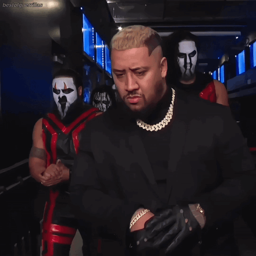 Man In Suit Standing Before Masked Wrestlers GIF