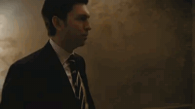 Man In Suit Standing By Blackboard In Dark Room GIF