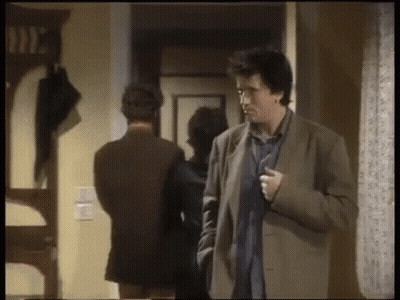 Man In Suit Standing In Hallway With Woman Behind Him GIF