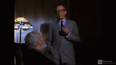 Man In Suit Standing Next To Man In Chair GIF