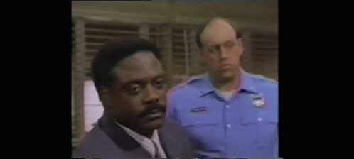 Man In Suit Standing Next To Police Officer In Blue Uniform GIF