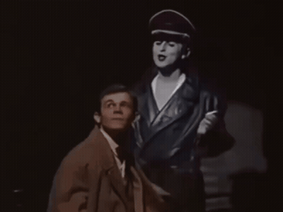 Man In Suit Standing Next To Woman In Hat GIF