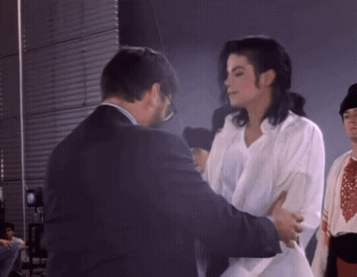 Man In Suit Standing Next To Woman In White Shirt GIF