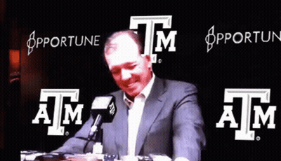 Man In Suit Talking Into Microphone In Front Of Apfortune Sign GIF