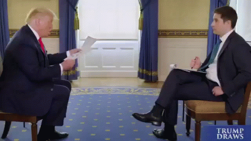 Man in Suit Talking to Man in Chair Trump Draws Sign