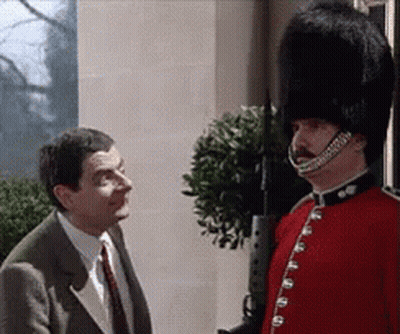 Man In Suit Talking To Man In Red Uniform And Black Hat GIF