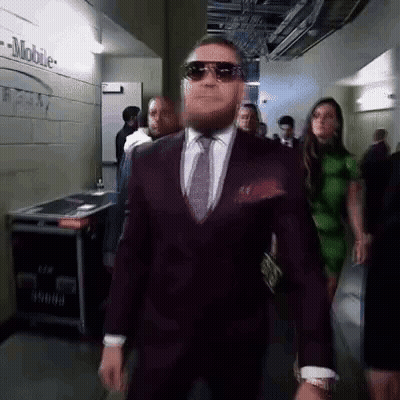 Man In Suit Walking Down Hallway With Group GIF