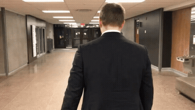 Man In Suit Walking Down Hallway With Water Fountain GIF