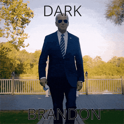 Man In Suit Walking In Front Of Dark Brandon Sign GIF