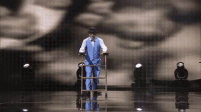 Man In Suit Walking On Stage With Cane And Ladder GIF