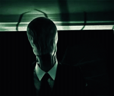 Man In Suit With Long Face Sitting In Dark Room GIF