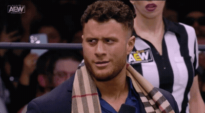 Man In Suit With Scarf And Woman In Striped AEW Shirt GIF