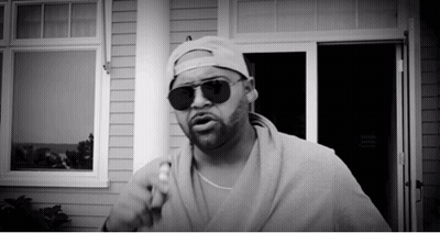 Man In Sunglasses And Baseball Cap Standing In Front Of House GIF