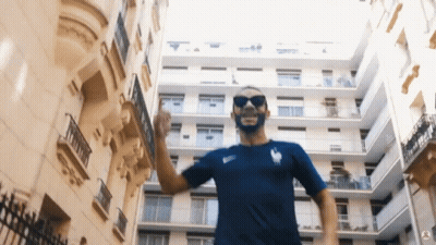 Man In Sunglasses And Blue Shirt In Front Of Building GIF