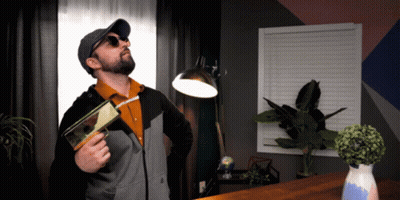 Man In Sunglasses And Hat Holding Book And Lamp GIF