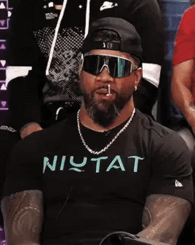 Man In Sunglasses And Hat Smoking Cigarette In Crowd GIF