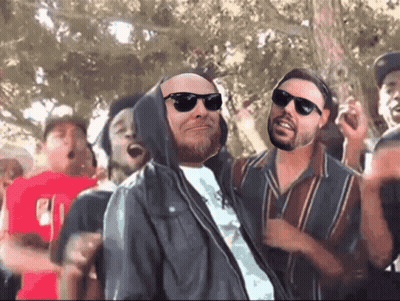Man In Sunglasses And Hooded Jacket In Crowd GIF