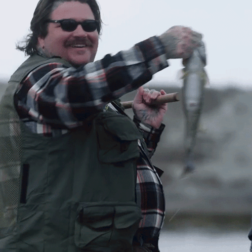 Man In Sunglasses And Plaid Shirt Holding Fish On Stick GIF