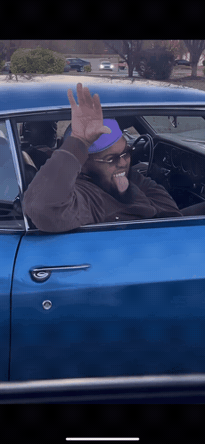 Man In Sunglasses And Purple Hat Waving From Blue Car GIF