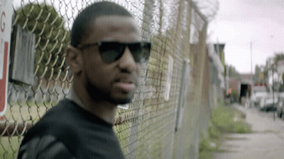 Man In Sunglasses Leaning Against Chain Link Fence GIF