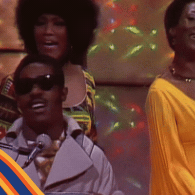 Man In Sunglasses Singing Into Microphone Woman In Yellow Dress Behind GIF
