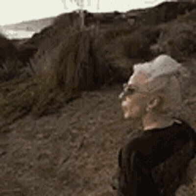 Man In Sunglasses Standing On Dirt Path Looking At Ocean GIF