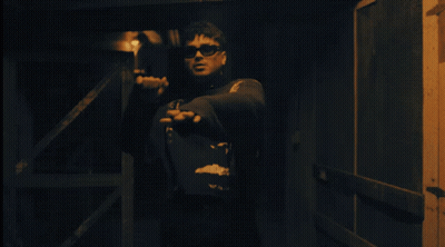 Man In Sunglasses Standing With Hands Outstretched In Dark Room GIF