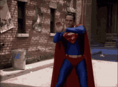 Man In Superman Costume In Front Of Brick Building GIF