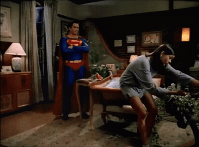 Man In Superman Costume Next To Woman In Grey Sweater GIF