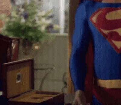 Man In Superman Costume Standing Next To Cigar Box GIF