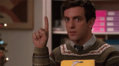 Man In Sweater And Tie Holding Book Pointing Up GIF