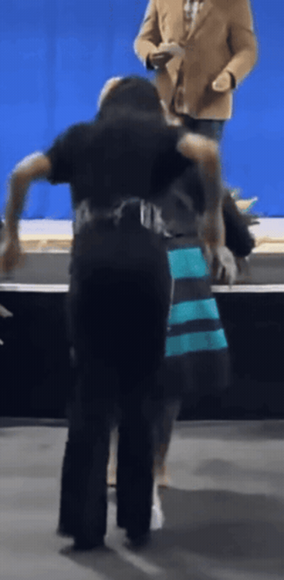 Man in Tan Jacket Behind Woman in Blue and Black Dress