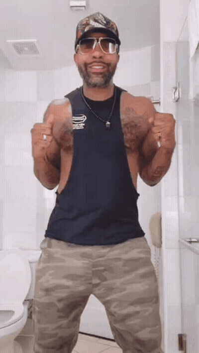 Man In Tank Top And Camo Pants Giving Two Thumbs Up In Bathroom GIF