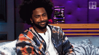 Man In Tie Dye Jacket Smiling On Bed GIF