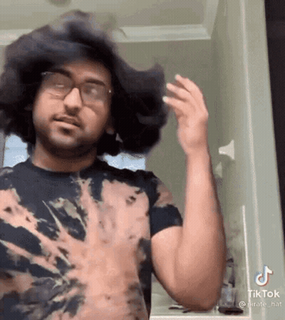 Man In Tie Dye Shirt Standing In Front Of Mirror GIF