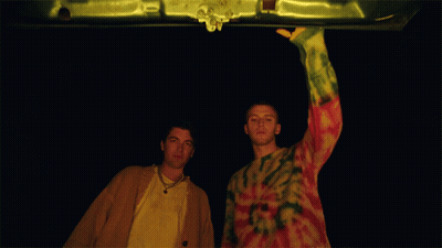 Man In Tie Dye Sweater Next To Man In Yellow Jacket GIF