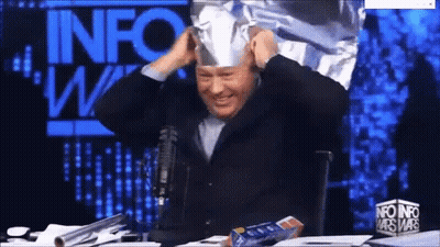 Man In Tin Foil Hat In Front Of Info Wars Sign GIF