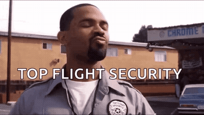 Hombre con Uniforme de Seguridad Top Flight de Pie Frente a un Edificio GIF