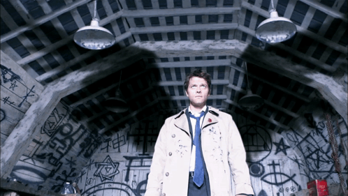 Man In Trench Coat And Tie In Dark Room With Graffiti GIF